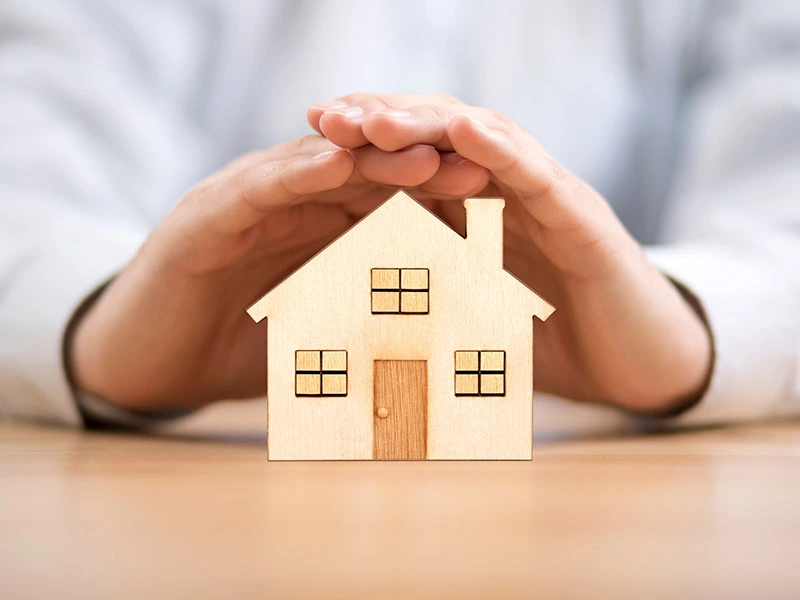 Wooden toy house protected by hands. Home insurance concept