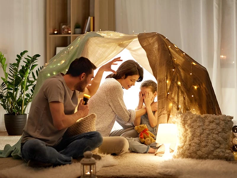 father with torch light telling scary stories to his daughter and wife in a fort