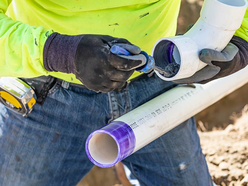 Plumber Applying Pipe Cleaner, Primer and Glue to PVC Pipe At Home Construction Site
