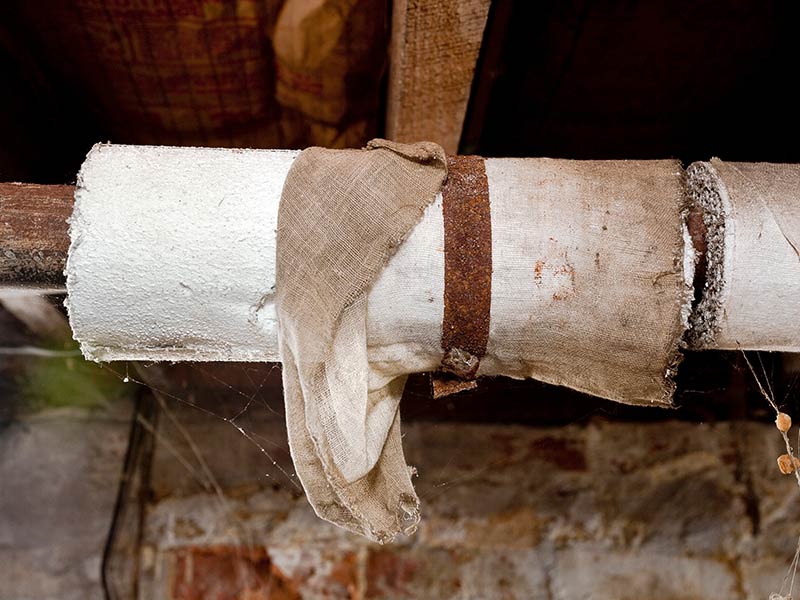 Basement plumbing pipes wrapped with asbestos insulation
