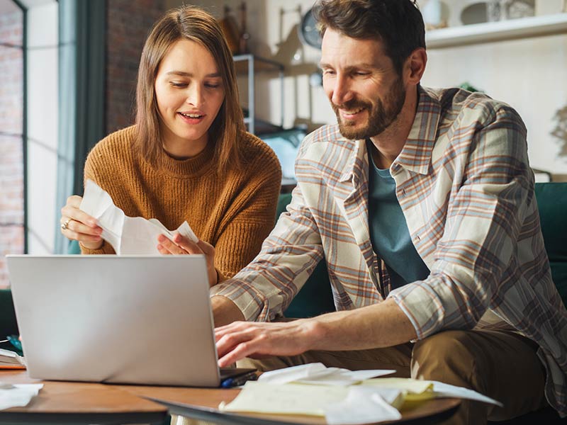Happy Couple Using Laptop Computer, Sitting on Sofa in Apartment after restoration