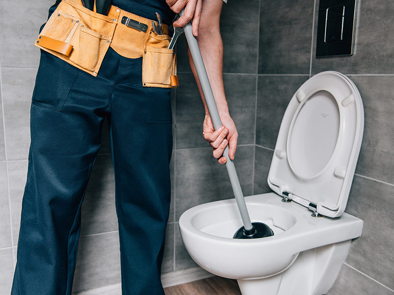 partial view of male plumber using plunger in toilet in bathroom