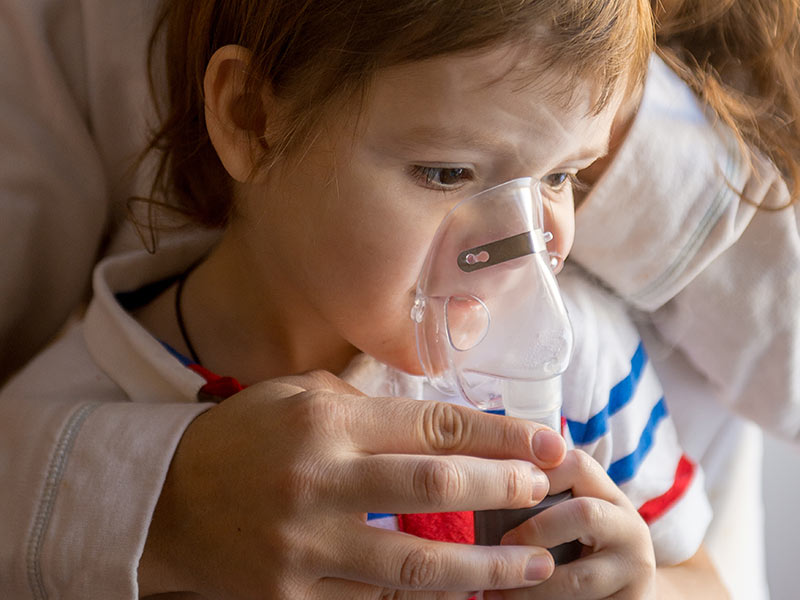 Young woman with son doing inhalation a nebulizer at home